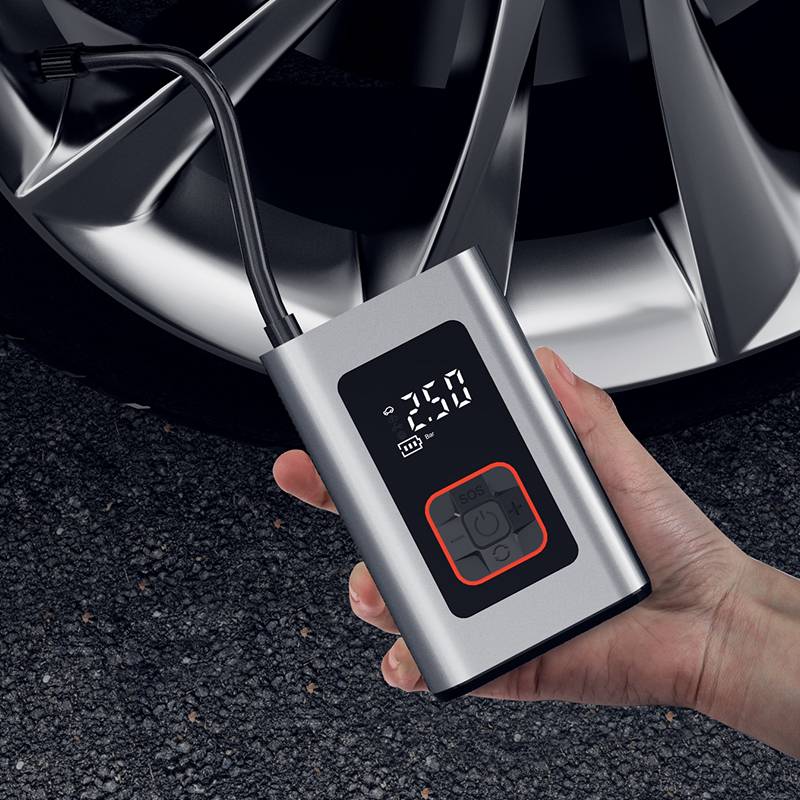 Hand holding BCA portable digital tire inflator checking car wheel pressure on asphalt surface

